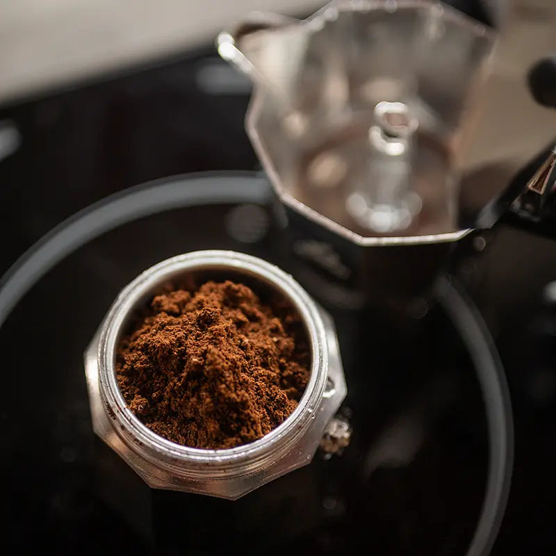 Frisch gemahlenes Espressopulver im Siebträger neben Espressokocher