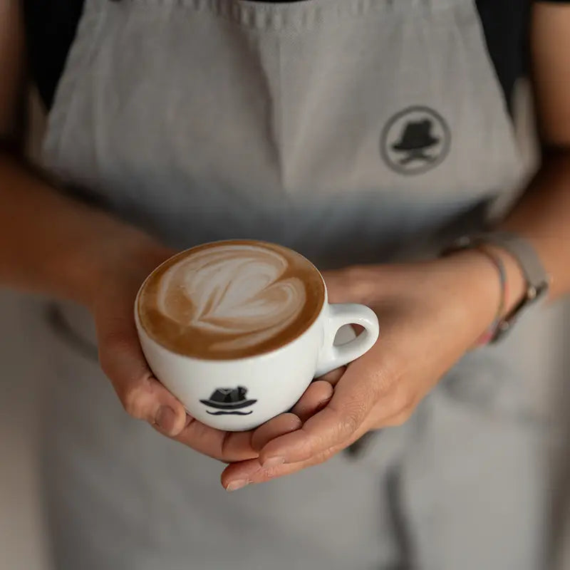 Kuntrawant Caffee Cappuccino mit Herz-Latte-Art in Barista-Hand gehalten